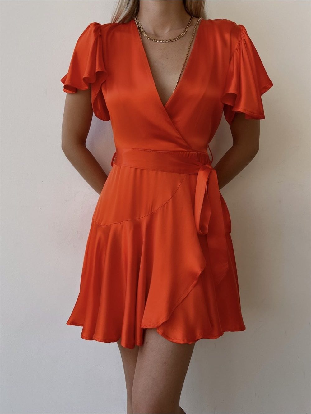 woman wearing a satin burnt orange dress with a short pleated sleeve and a skirt which is above knee height
